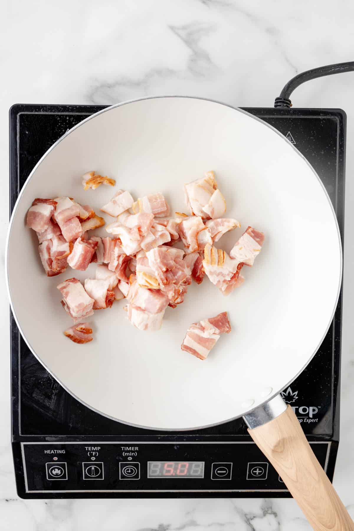 Chopped uncooked bacon in a white pan.