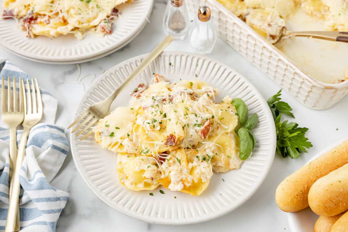 A plate of copycat Olive Garden ravioli carbonara next to breadsticks.