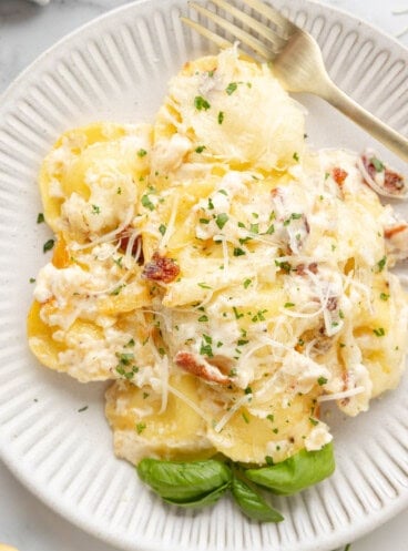 A close image of a plate of Olive Garden ravioli carbonara with fresh basil leaves and a fork.