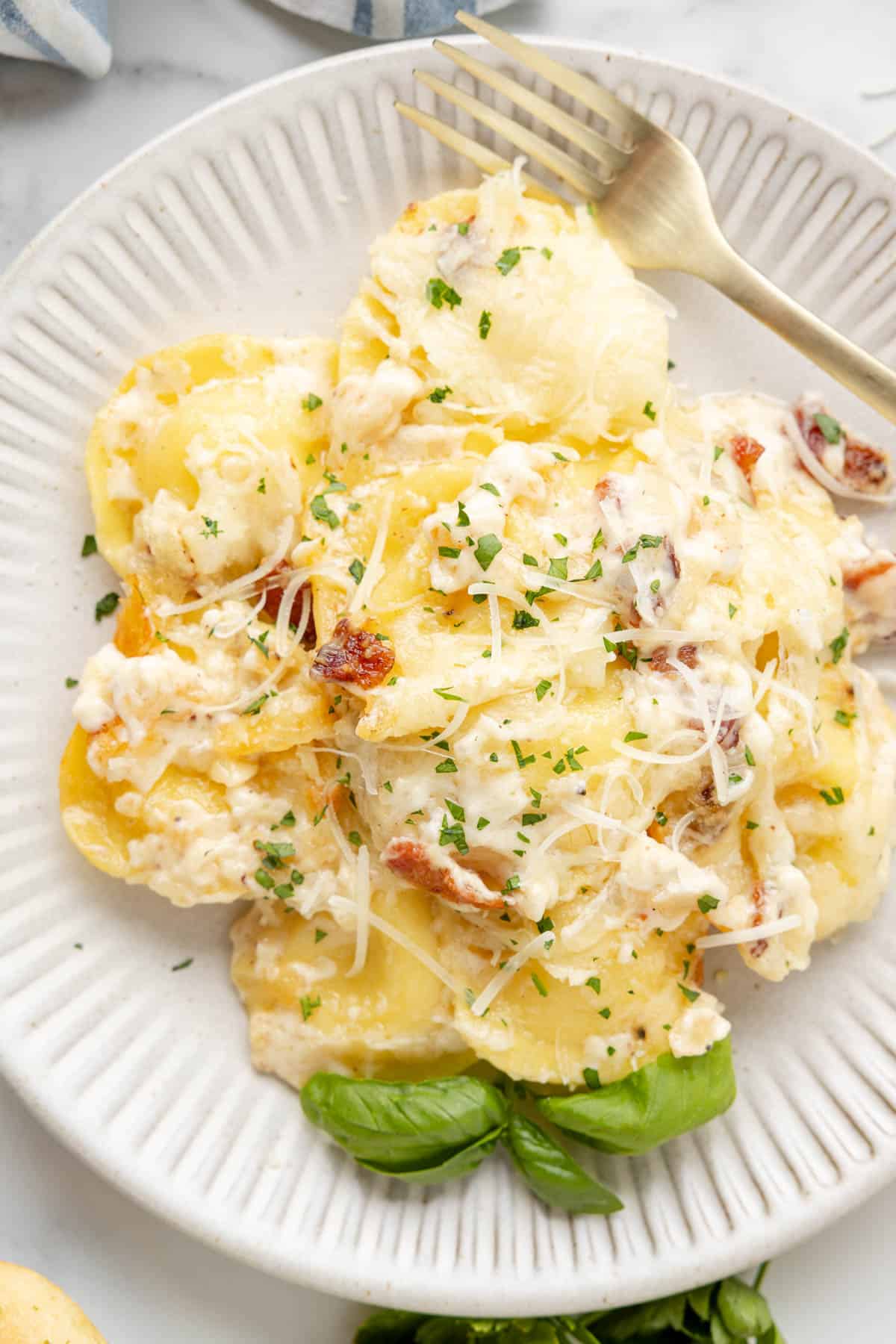 A close image of a plate of Olive Garden ravioli carbonara with fresh basil leaves and a fork.