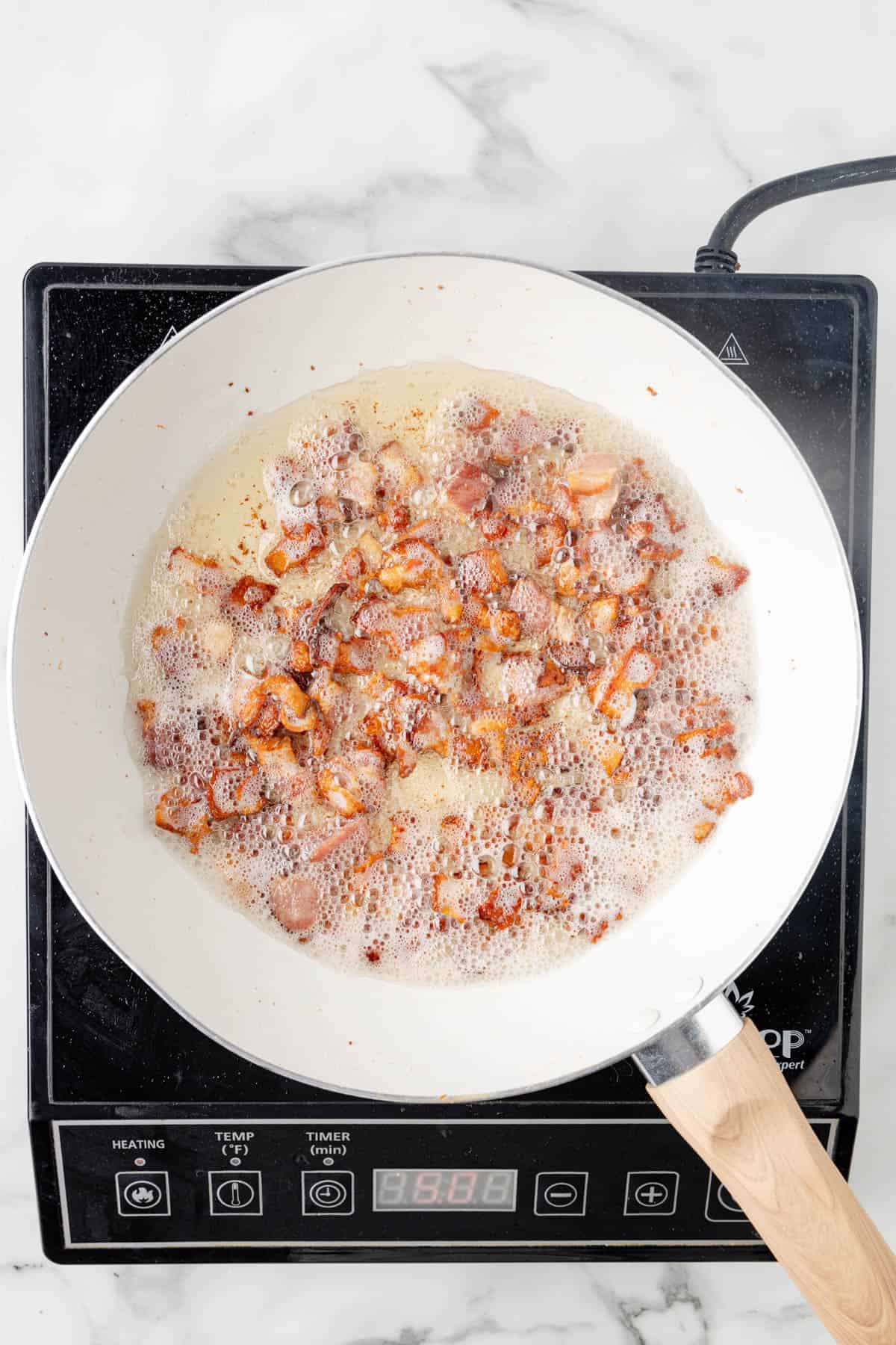 Bacon frying in hot oil in a skillet.