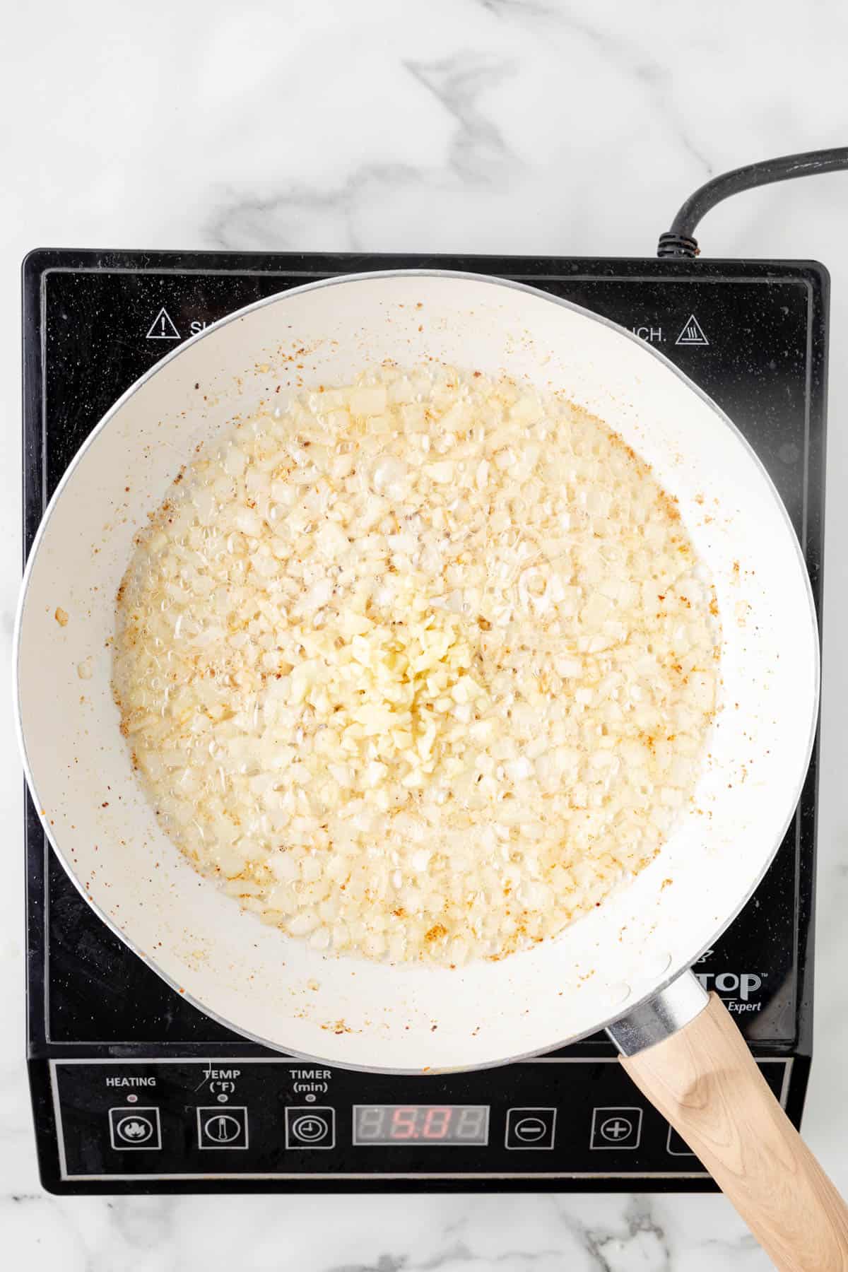 Adding minced garlic to sauteed onions in a pan.