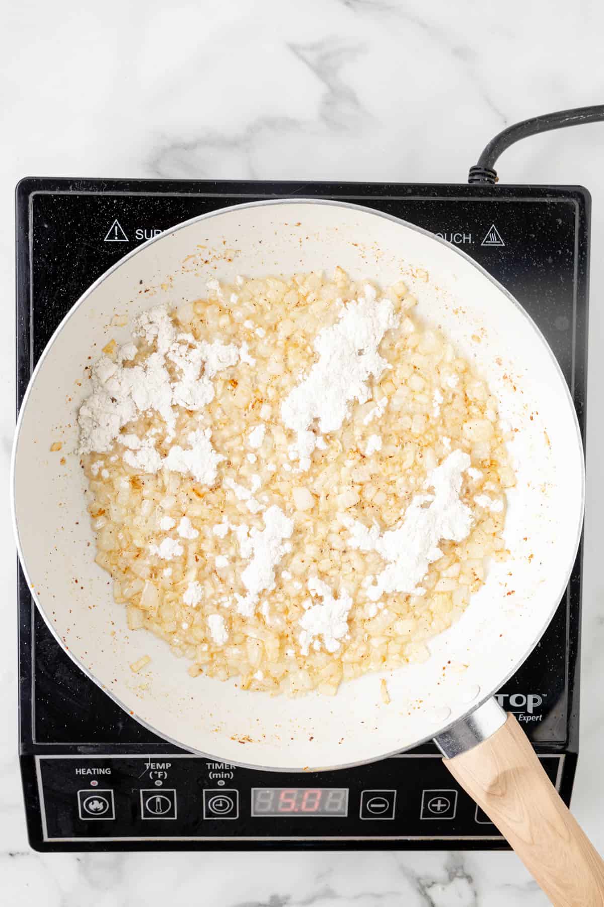 Adding flour to sauteed onions in a large skillet.