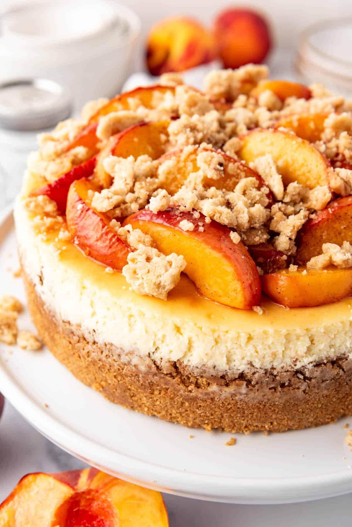 A side view of a New York style cheesecake with peaches on a white cake plate.