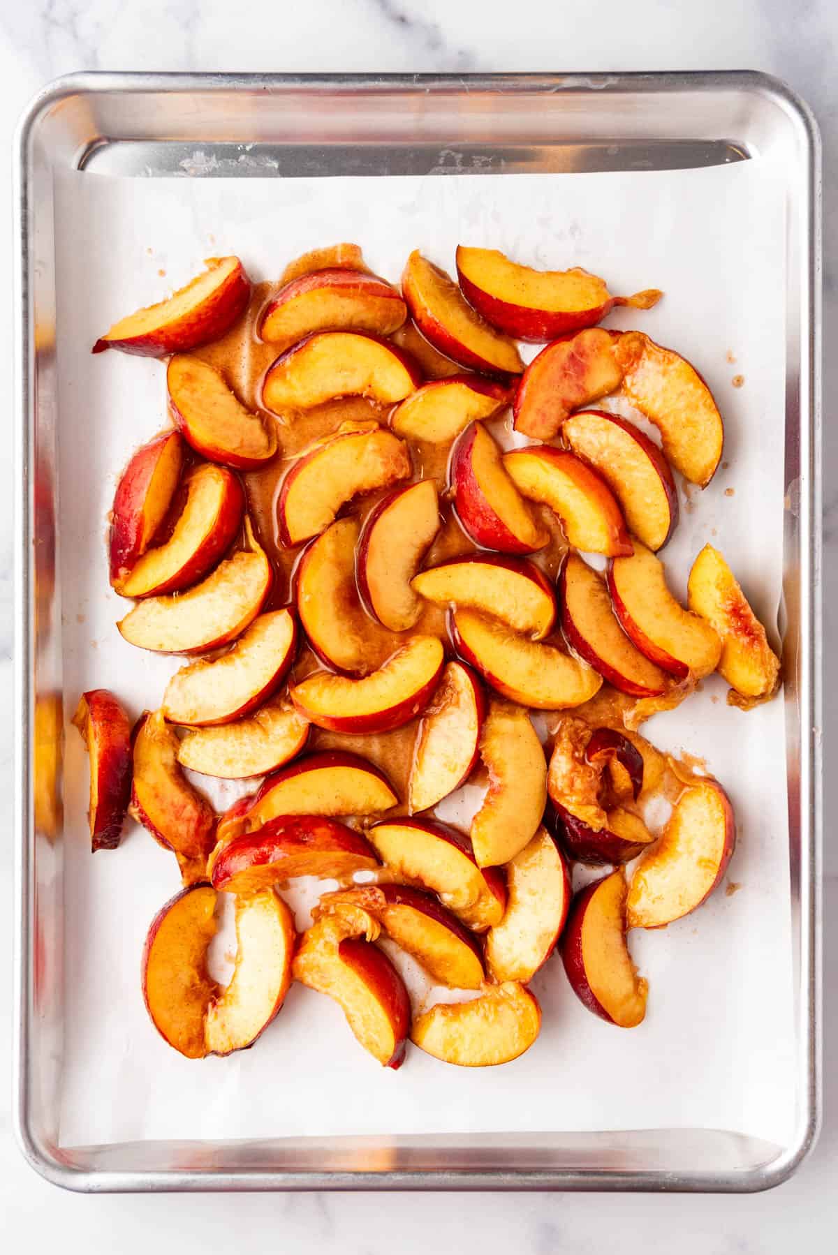 A baking sheet lined with parchment paper with sliced peaches on it.