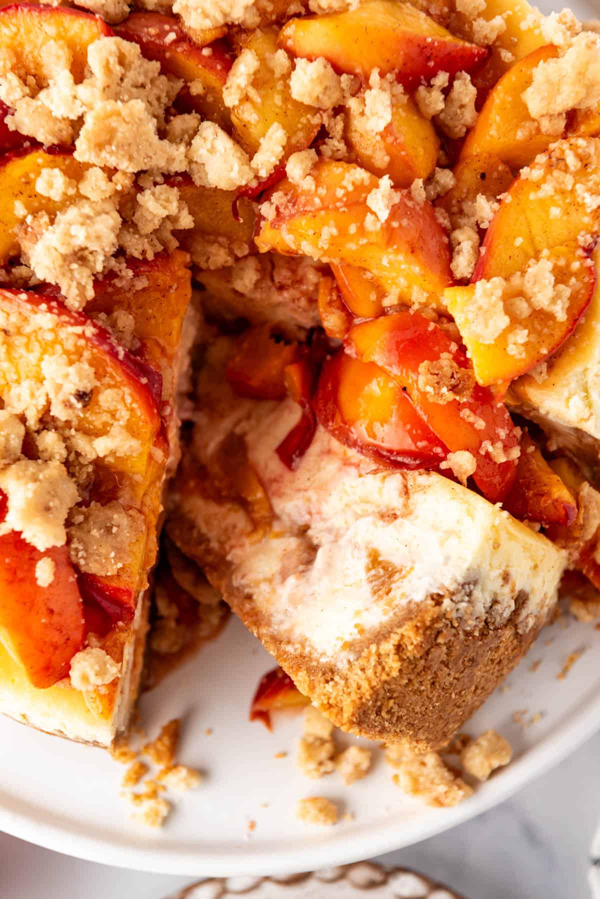 A slice of peach cobbler cheesecake laying on its side next to the rest of the cheesecake.