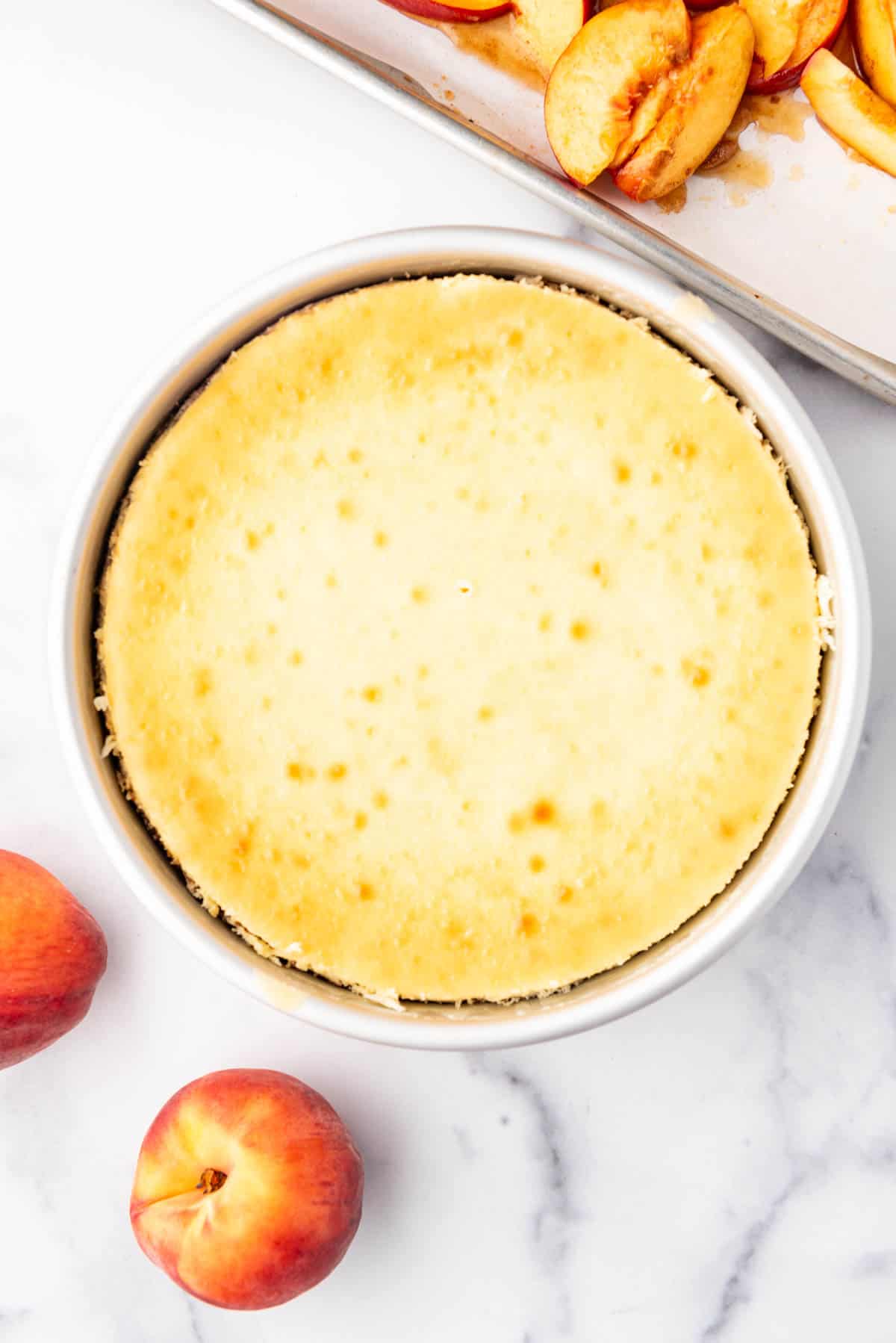 Un cheesecake cuit et prêt avant d'être décoré avec des pêches rôties et du crumble.