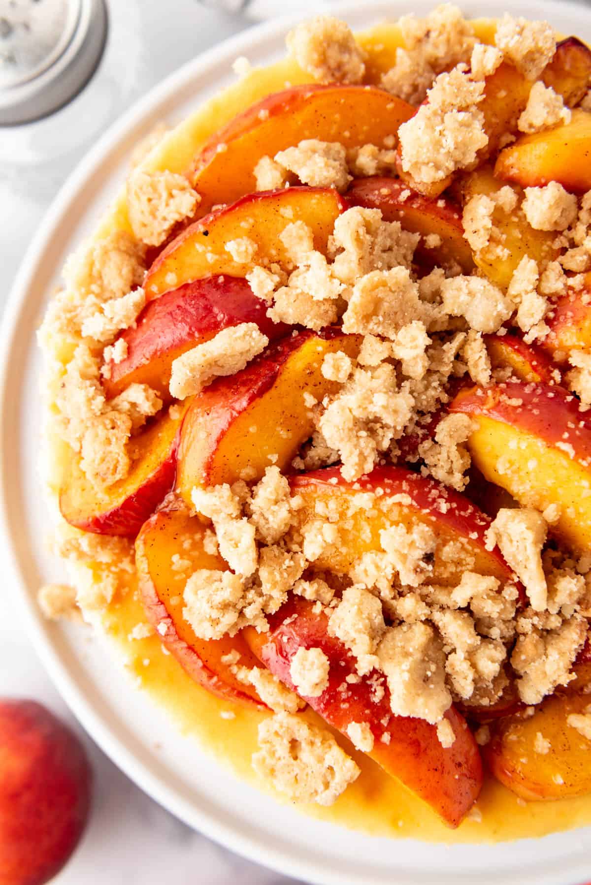 Une image en hauteur d’un cheesecake aux pêches fait avec des pêches fraîches et du crumble beurré.