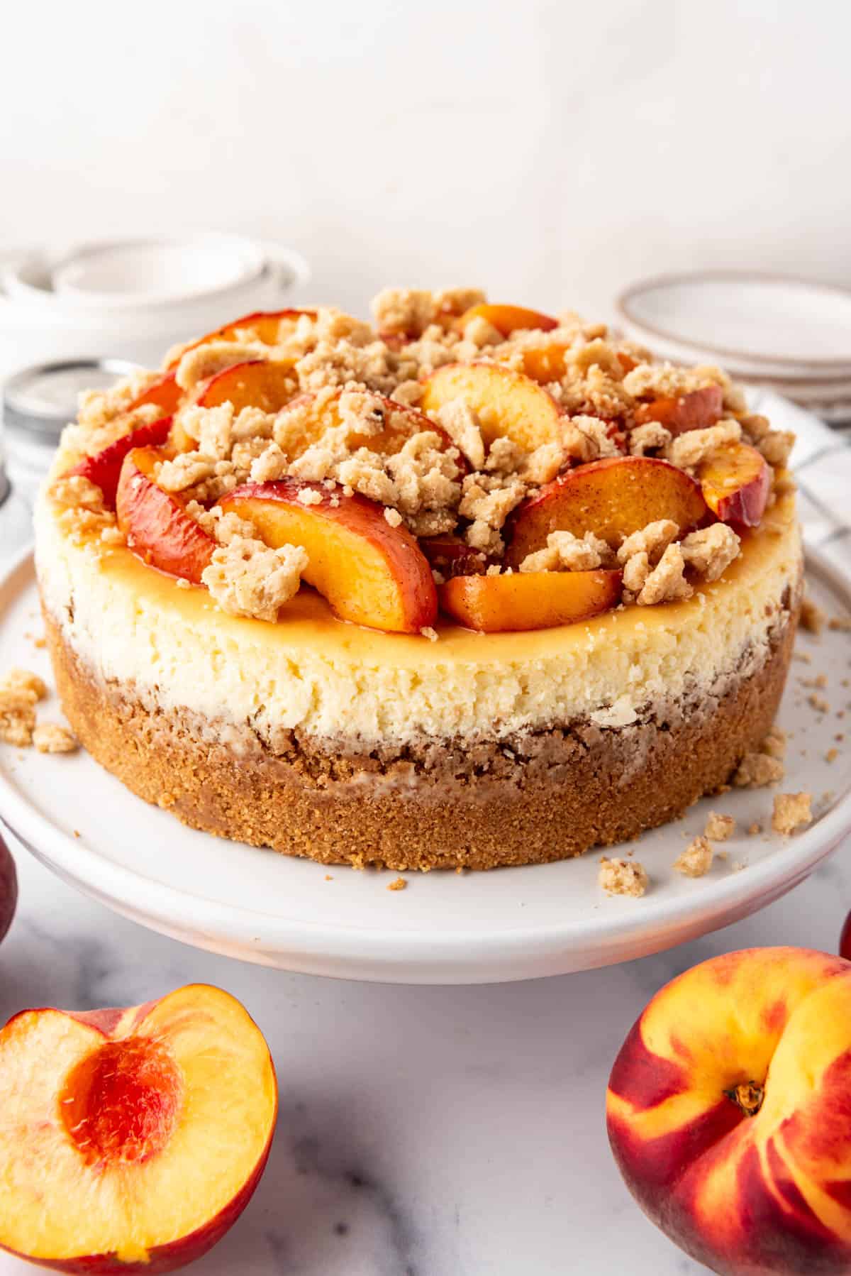 A full peach cobbler cheesecake on a white cake plate.