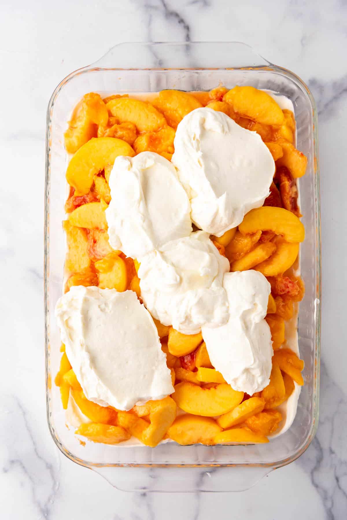 Adding more of the creamy filling on top of the sliced peaches layer.