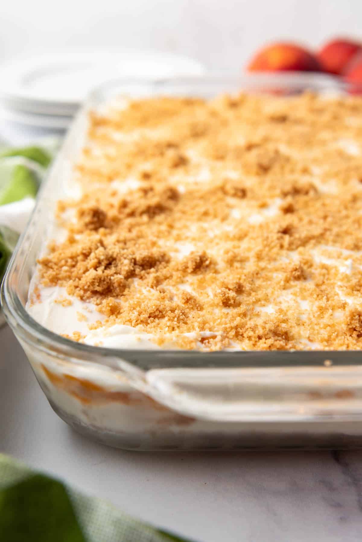 A side view of a layered peaches and cream dessert with graham cracker crumb topping.