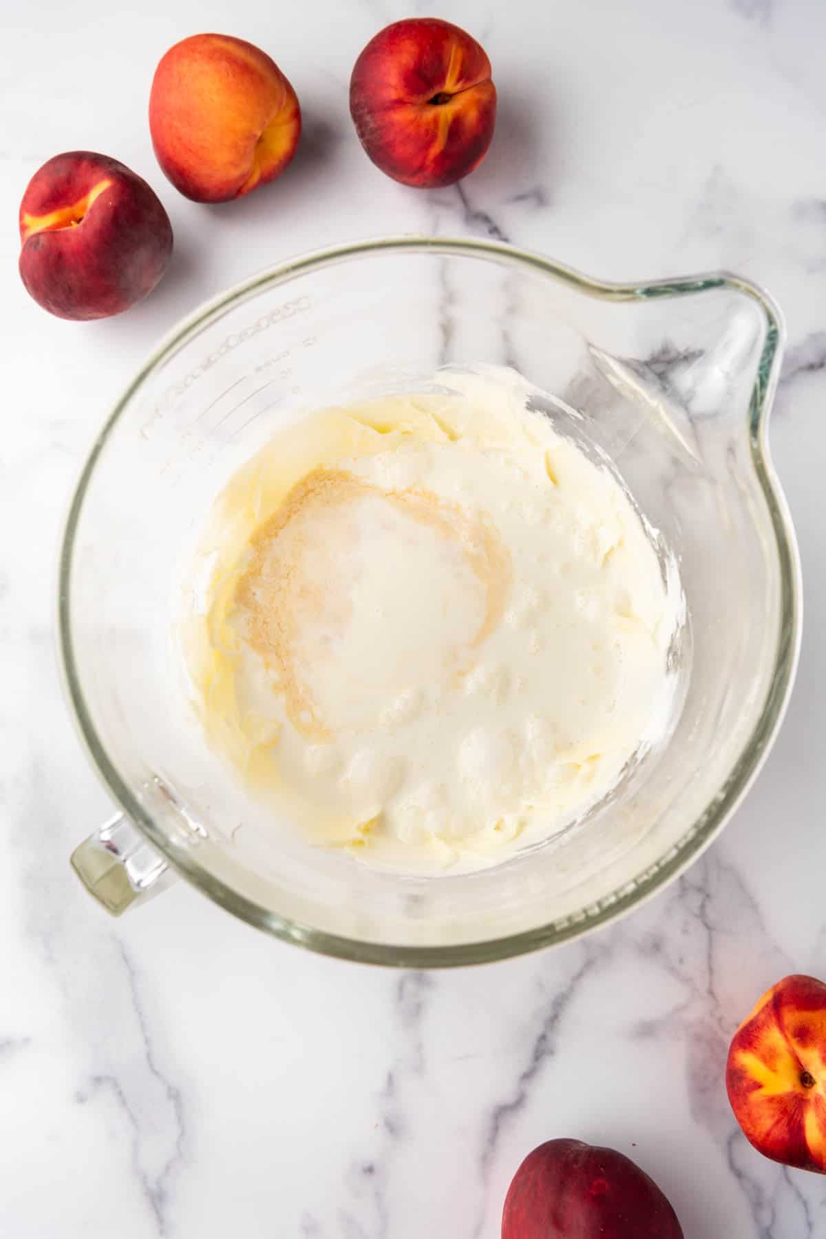 Adding heavy cream, vanilla extract, and almond extract to creamed cream cheese and powdered sugar.