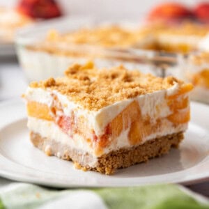 An image of a square slice of peaches and cream dessert on a white plate.