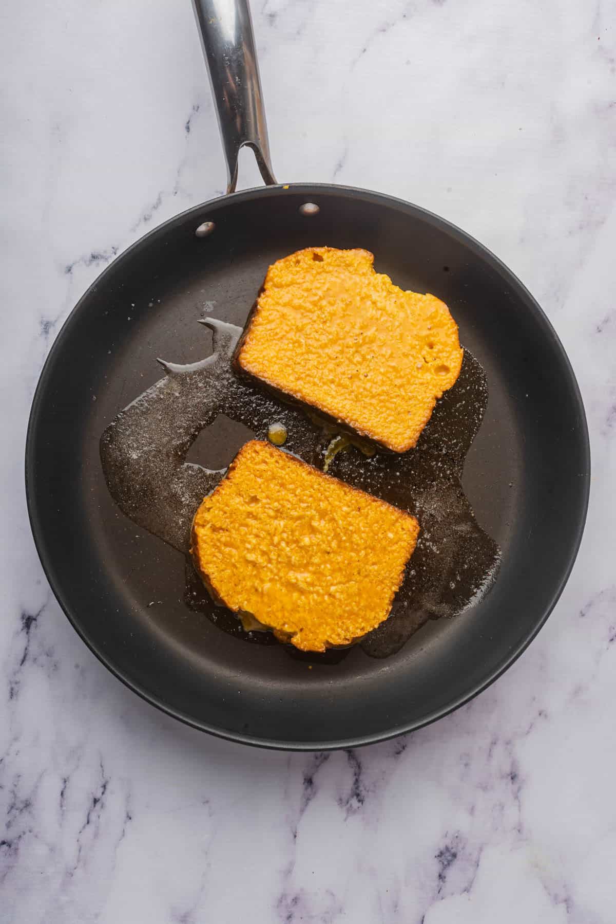 Cooking slices of pumpkin french toast in a little melted butter in a frying pan.