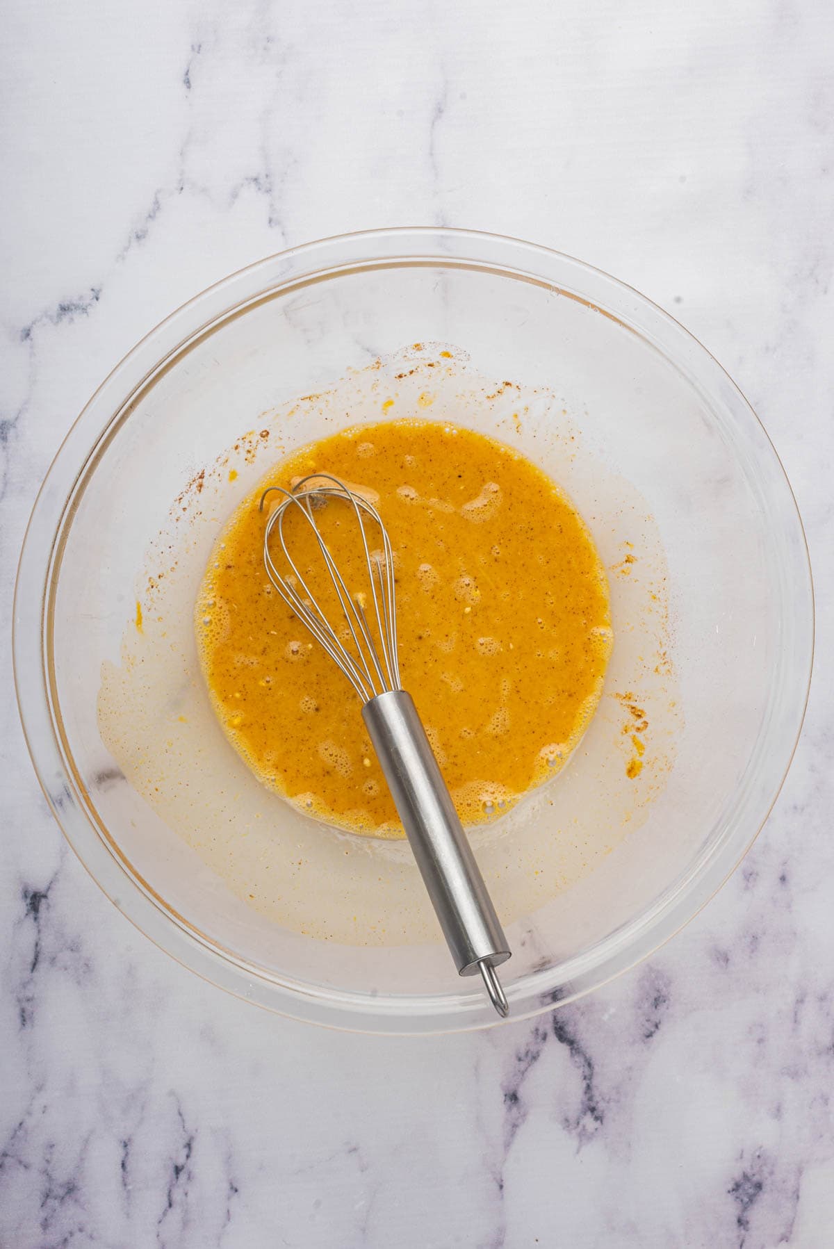 A whisk in a bowl of whisked egg, milk, pumpkin, spice, and brown sugar mixture for making french toast.