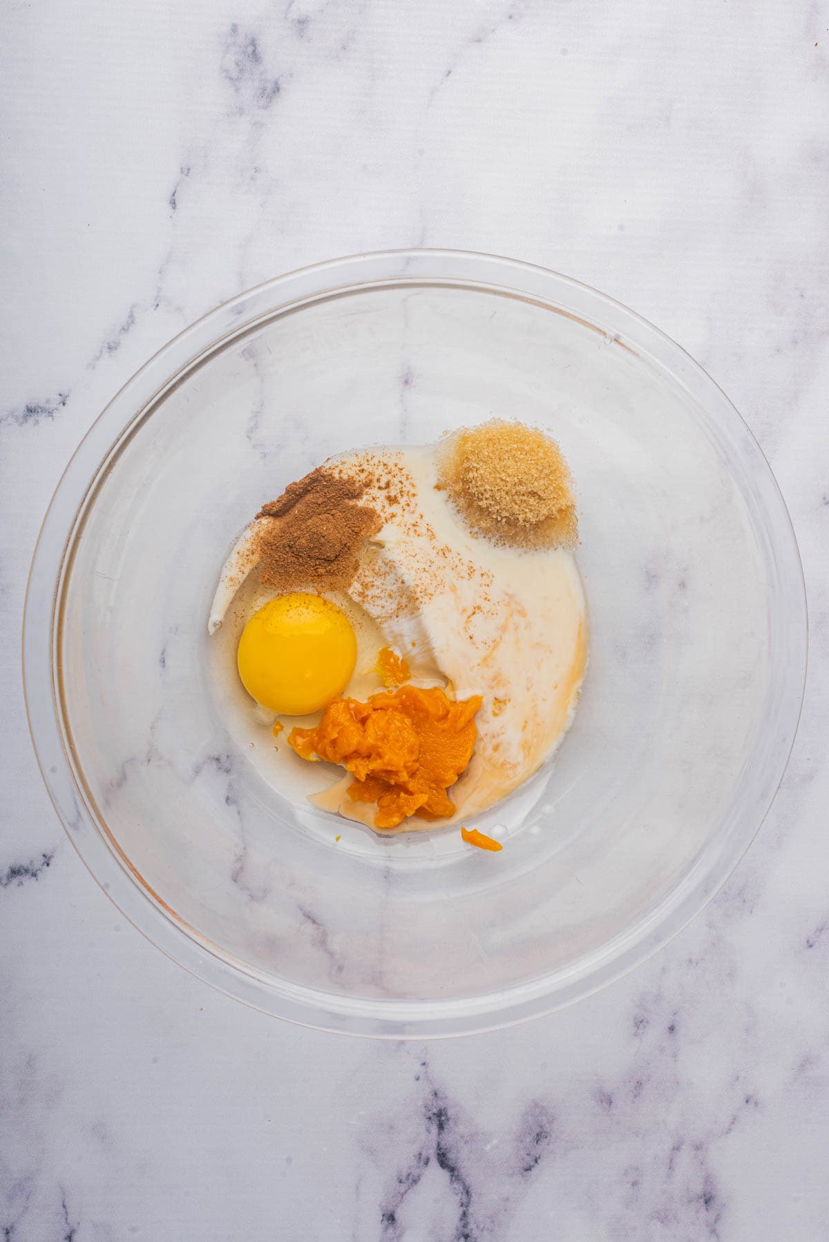 Combining ingredients in a large glass bowl to make pumpkin french toast.