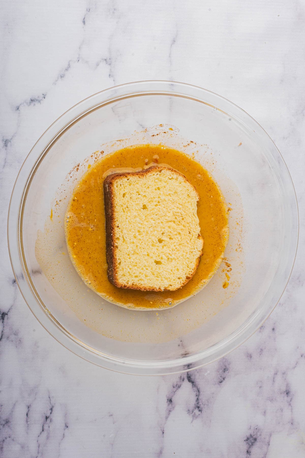 A slice of bread in a bowl of egg custard mixture for making pumpkin french toast.