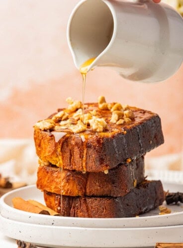 An image of syrup being poured over a stack of three slices of pumpkin french toast.