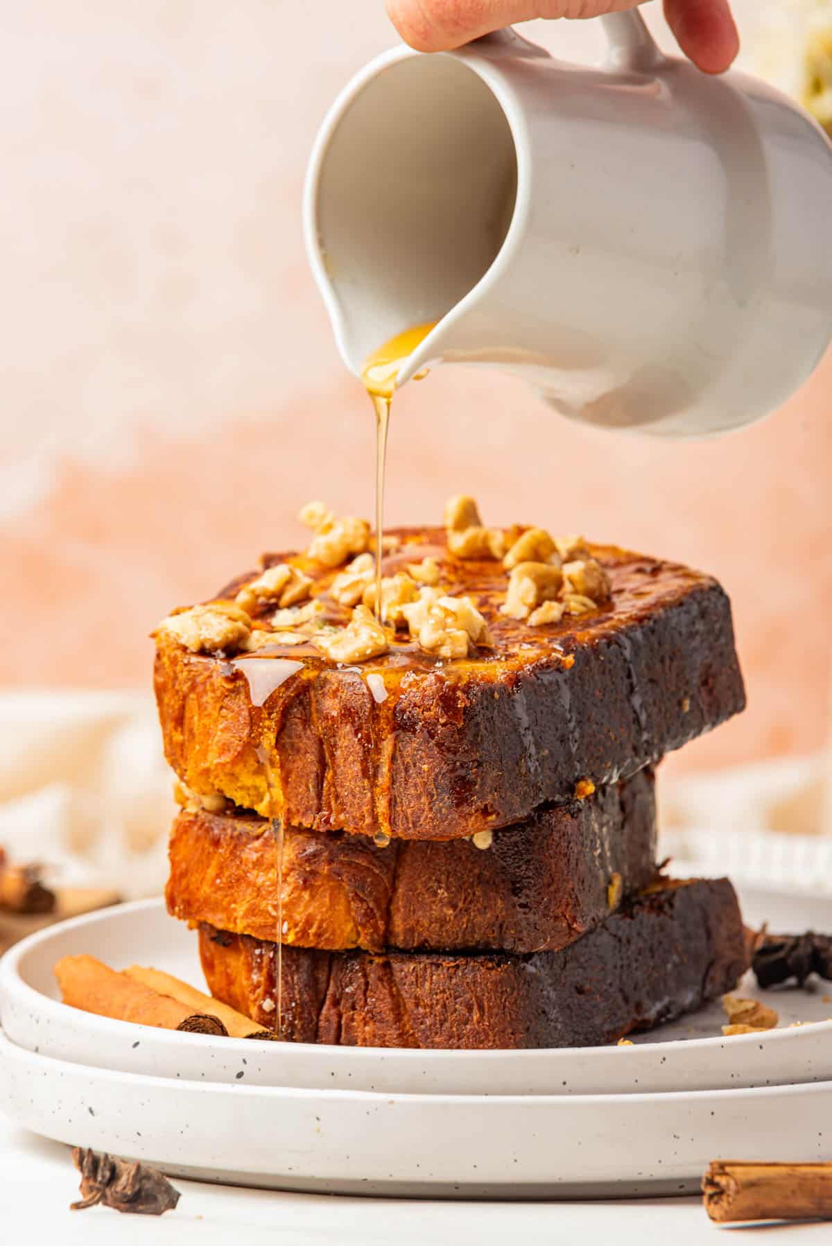 An image of syrup being poured over a stack of three slices of pumpkin french toast.