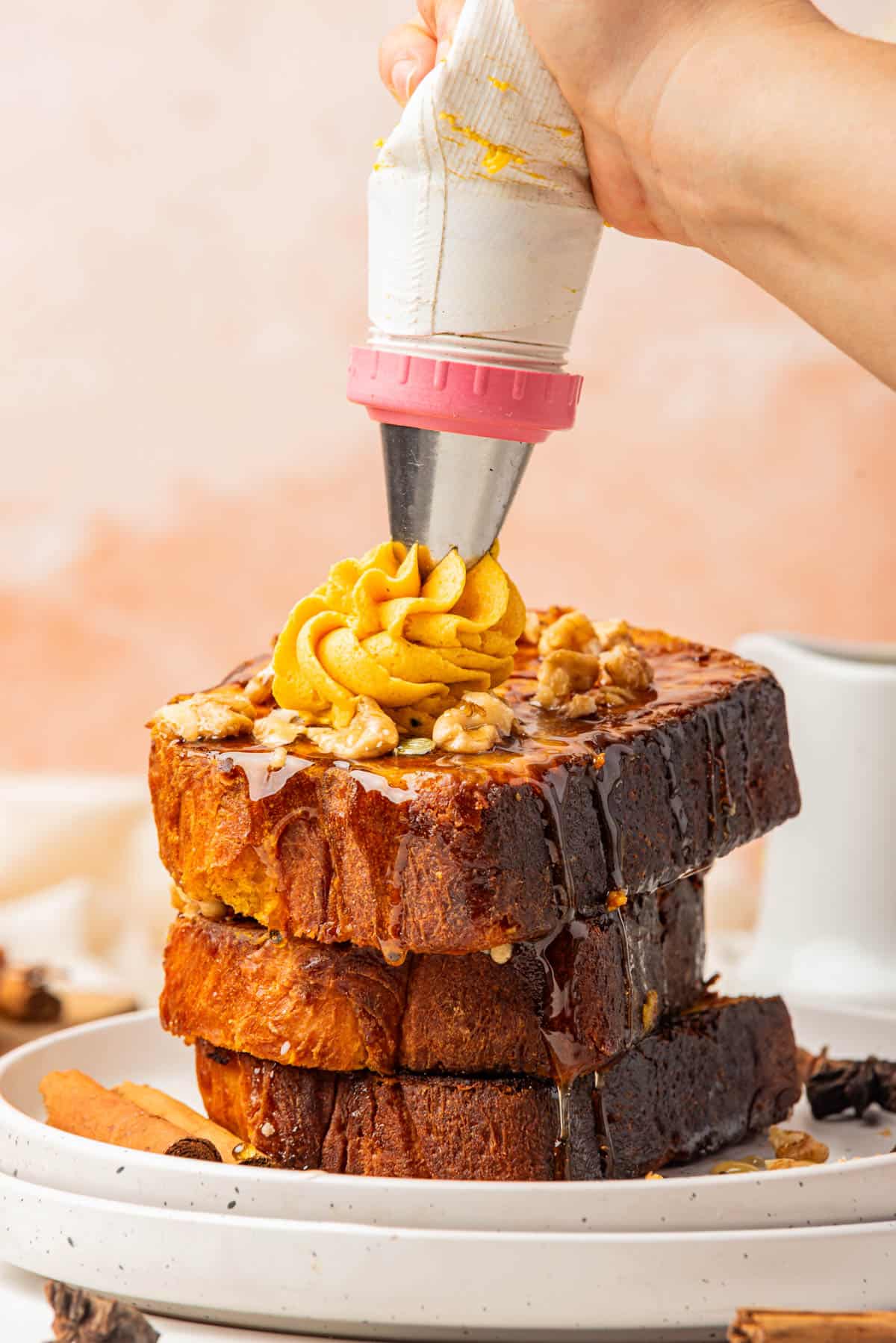 Piping swirls of pumpkin butter on top of a stack of pumpkin french toast.