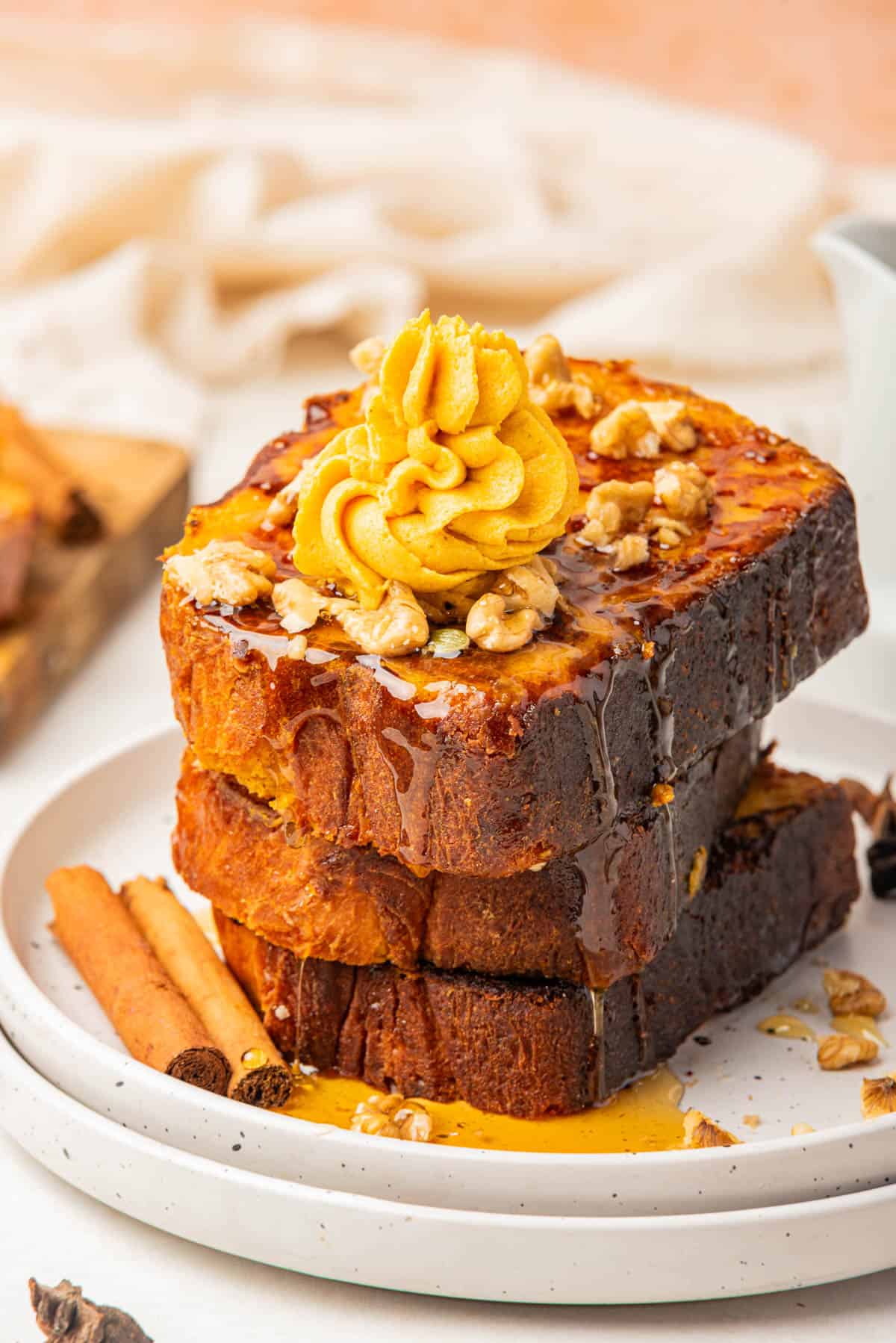 A stack of pumpkin French toast topped with syrup and pumpkin honey butter on a plate with cinnamon sticks.