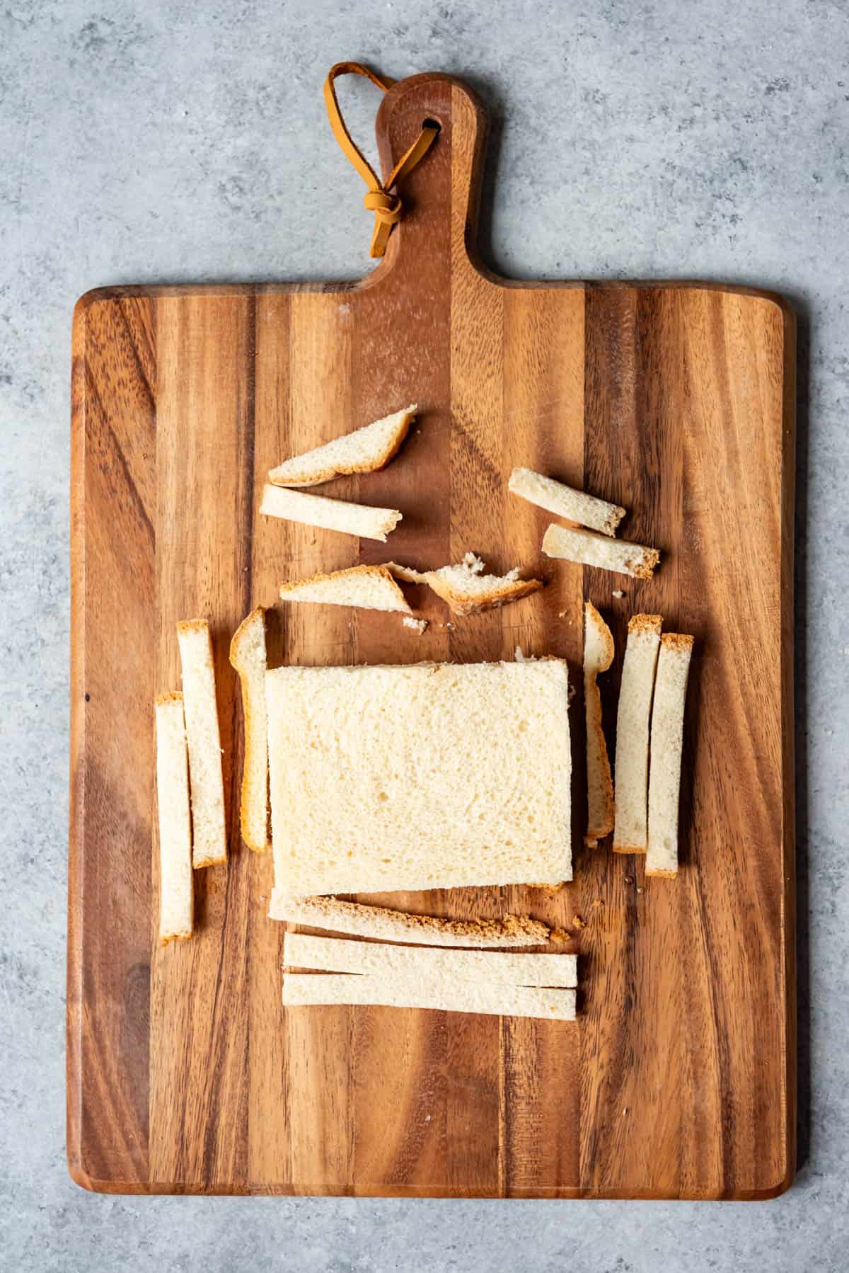 Cutting off crusts of bread on a wooden cutting board.