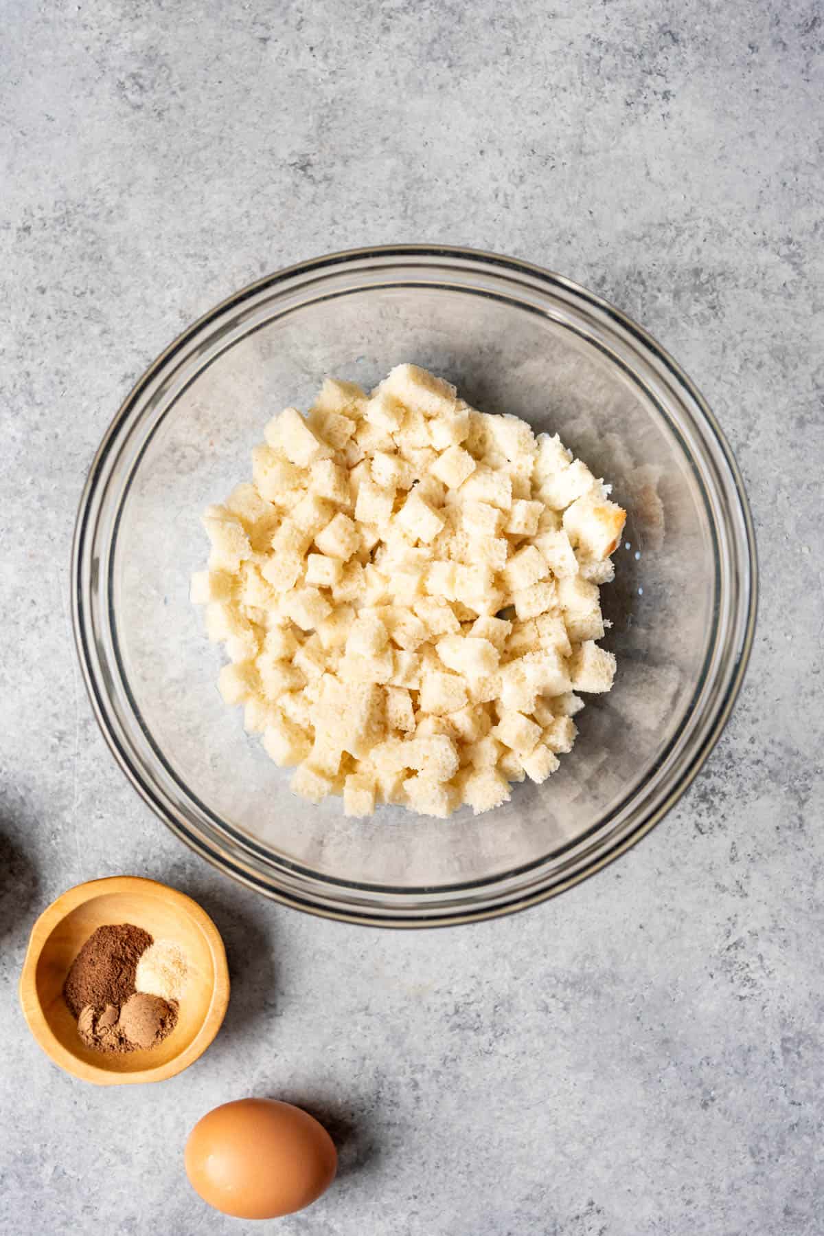 Soaking cubed white bread in milk in a glass mixing bowl.