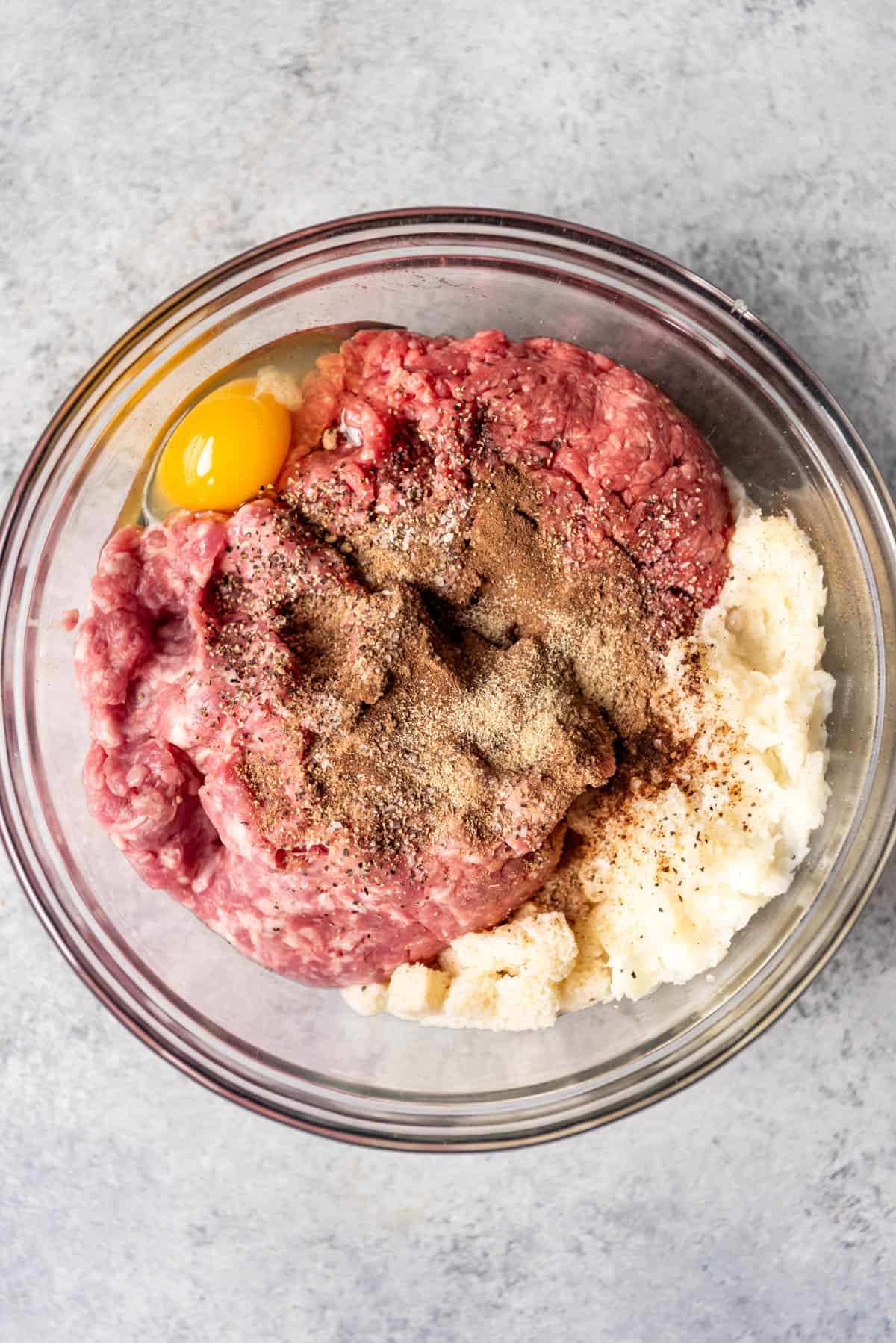 Combining ingredients for Swedish meatballs in a large glass bowl.