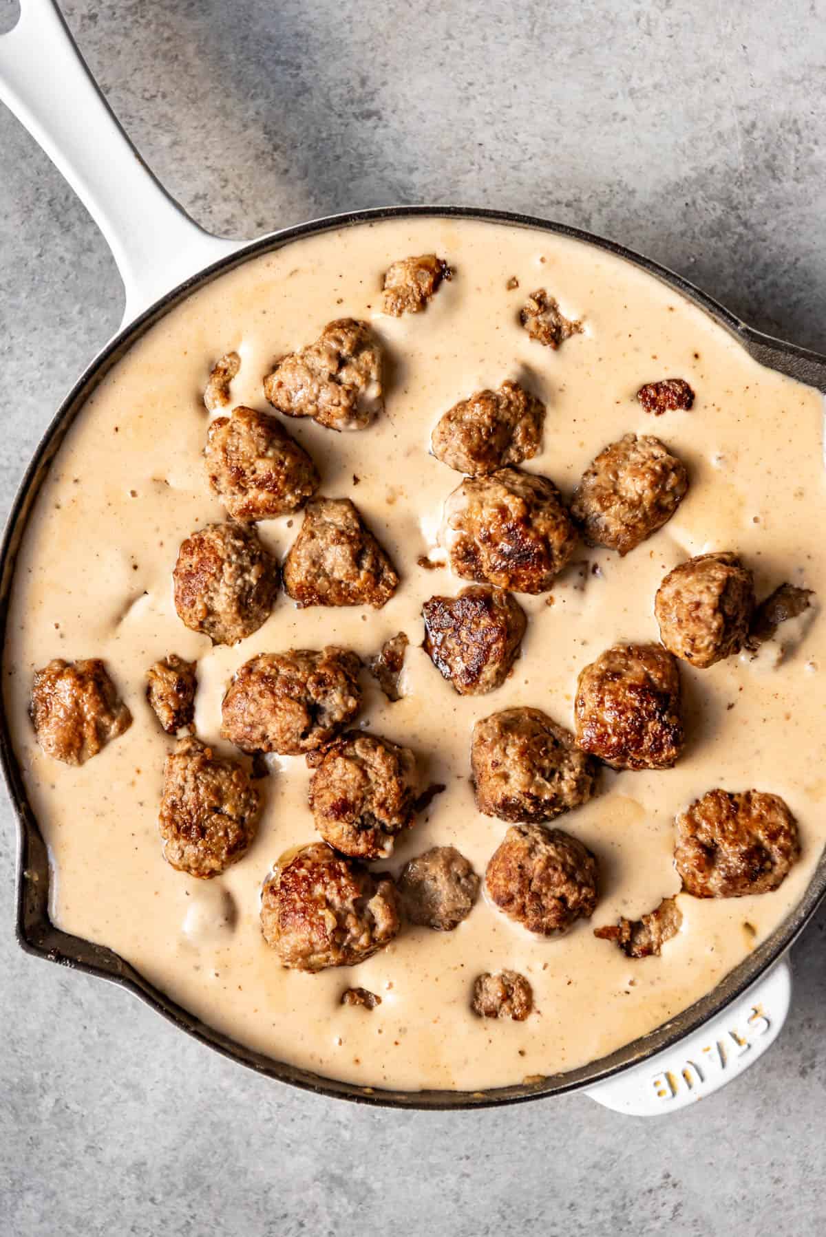 Adding baked meatballs to a creamy sauce in a large pan.