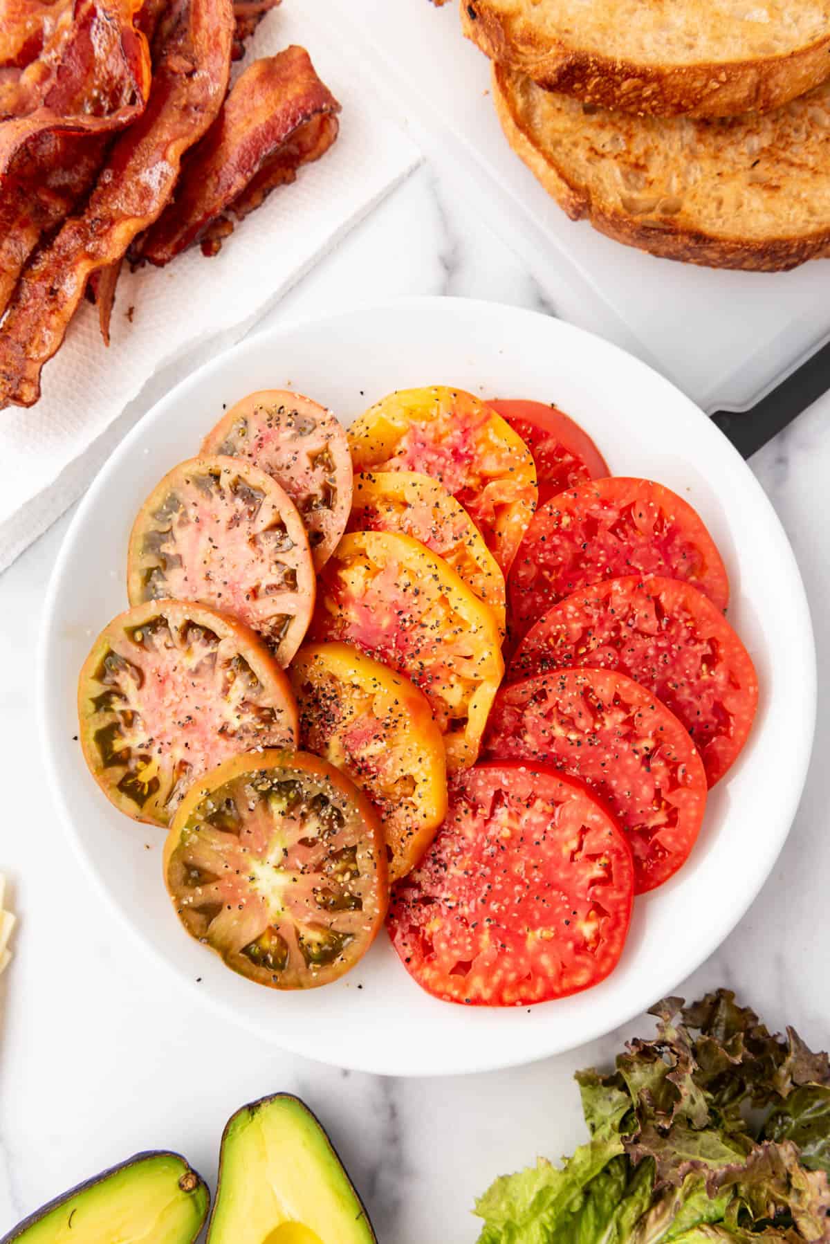 Sliced tomatoes on a white plate seasoned with salt and pepper.