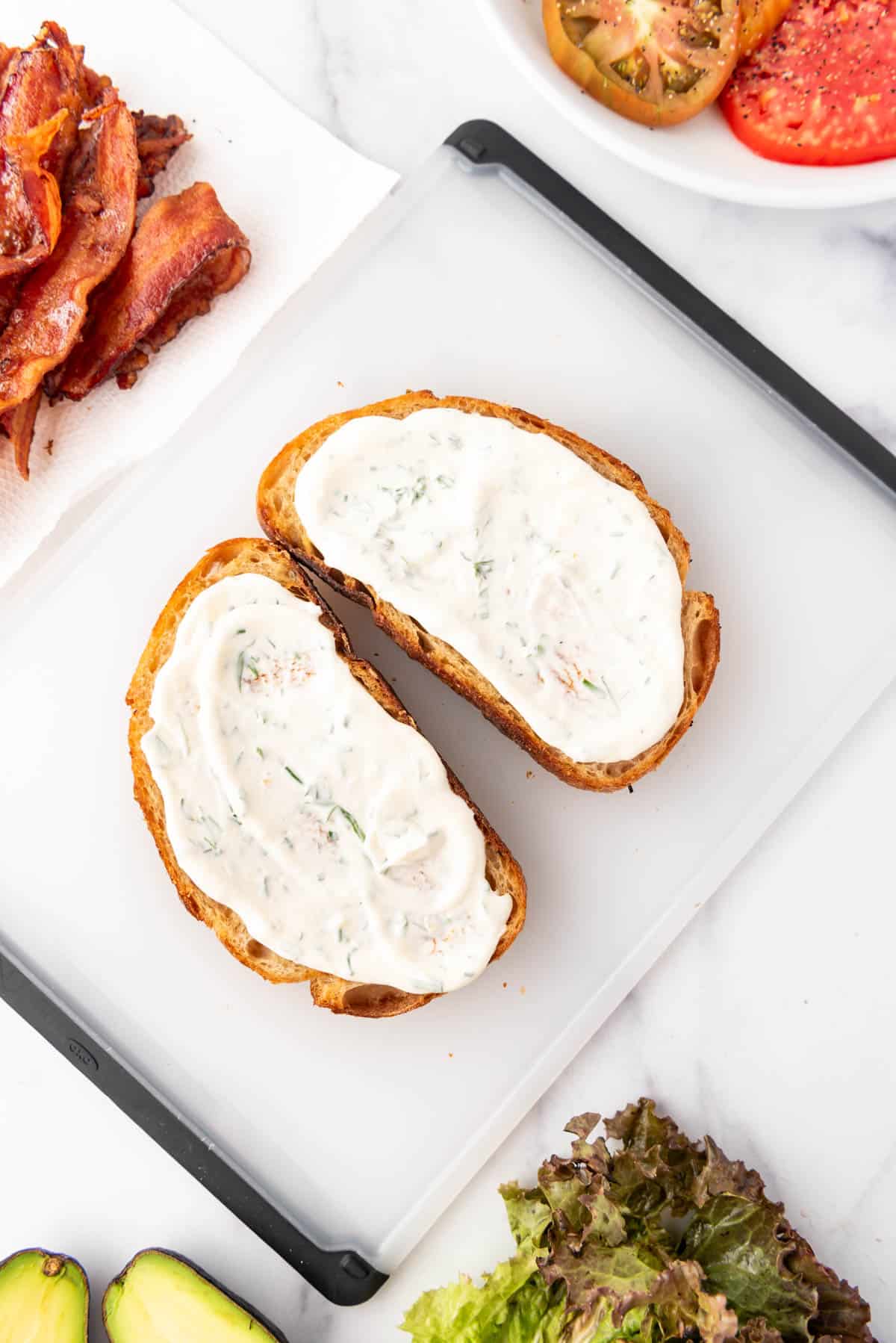 Spreading toasted bread with an herb mayo on a cutting board.