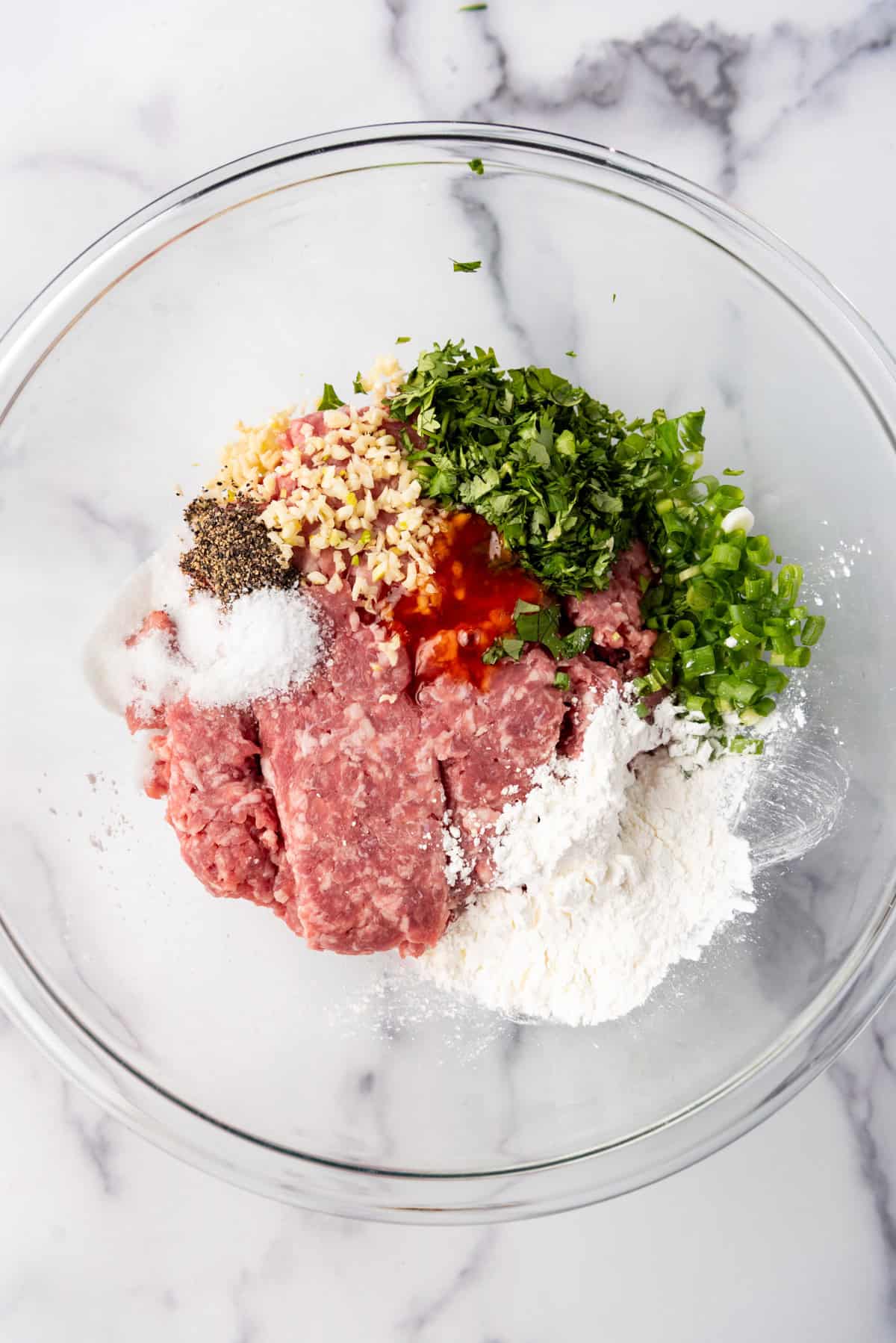 Combining  ingredients for banh mi meatballs in a glass mixing bowl.