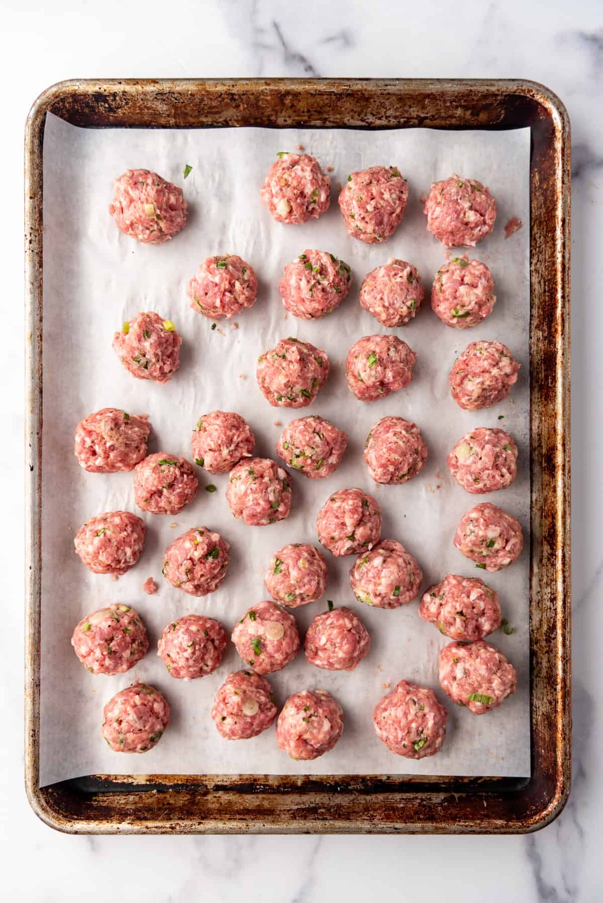 Uncooked meatballs on a baking sheet lined with parchment paper.