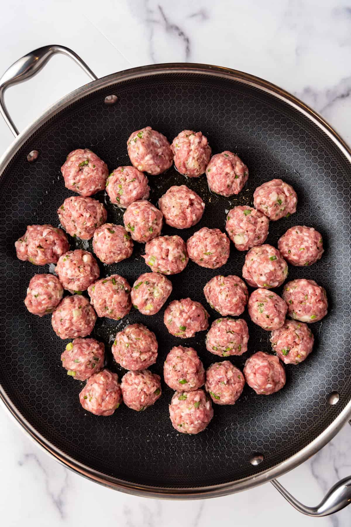 Searing meatballs for a banh mi in a large black skillet.