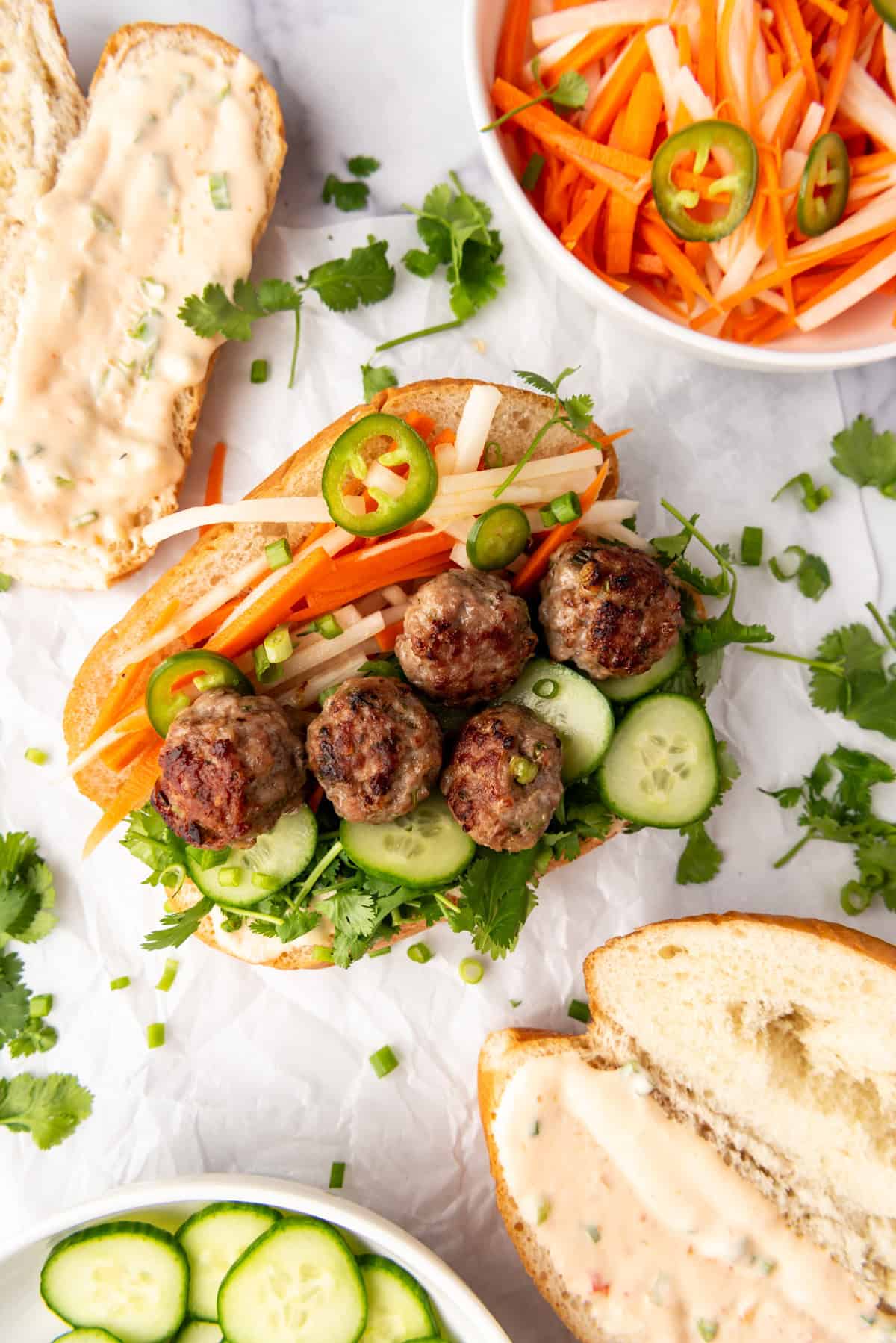 An assembled banh mi with Vietnamese-inspired meatballs next to soft bread and pickled vegetables.