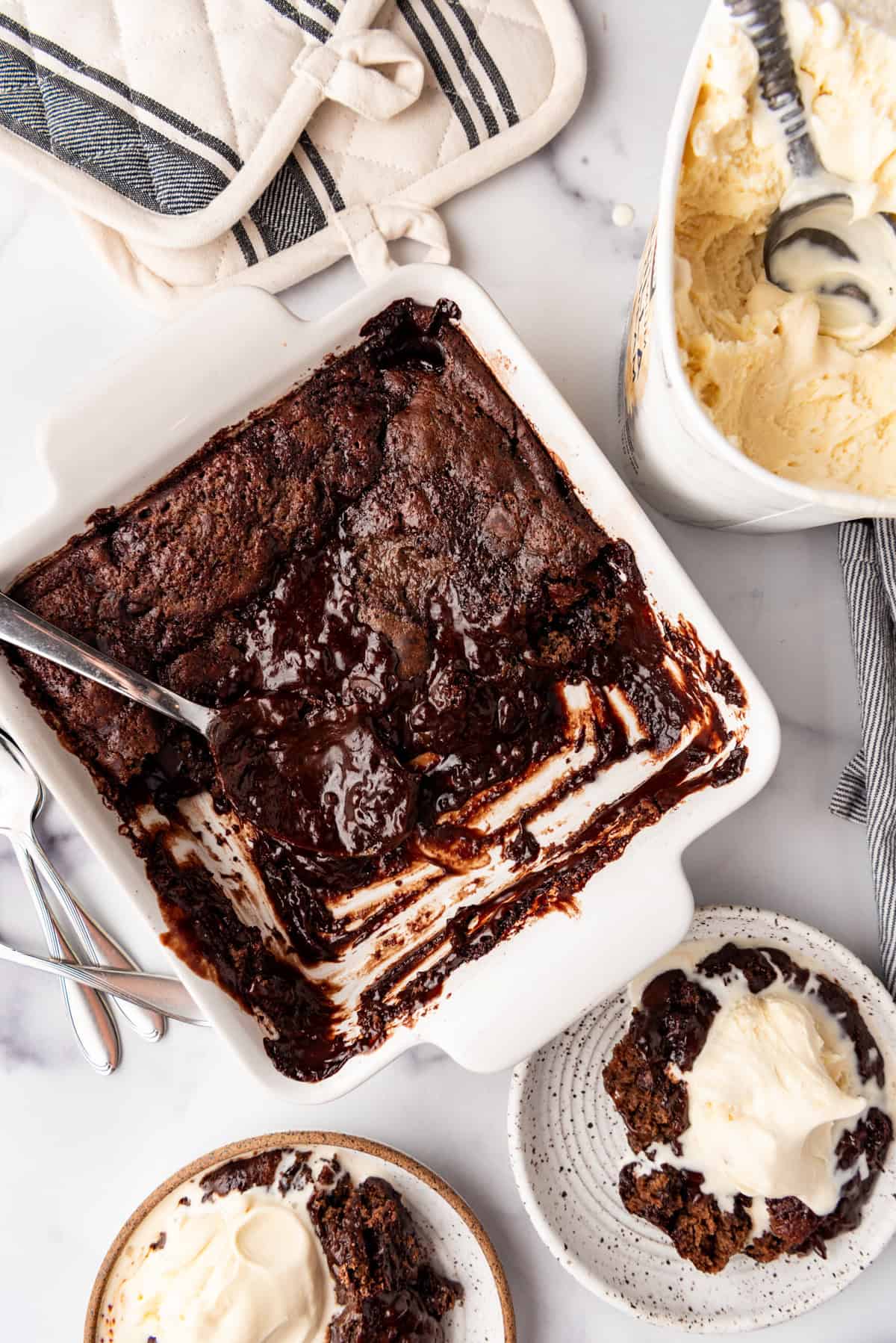 An overhead image of a chocolate cobbler in a square baking dish with a spoon in it.