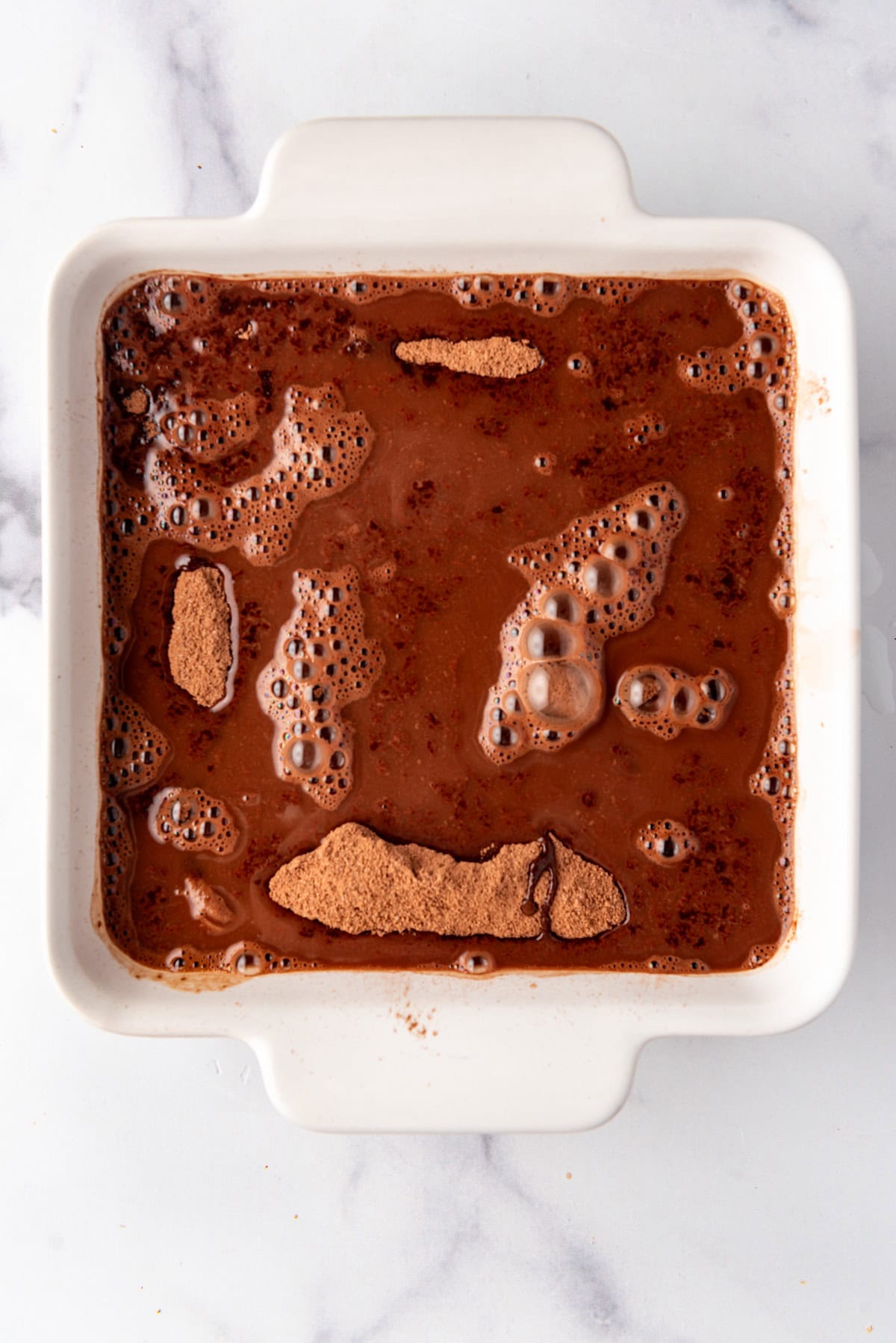 Boiling water poured over chocolate cobbler batter in a baking dish.