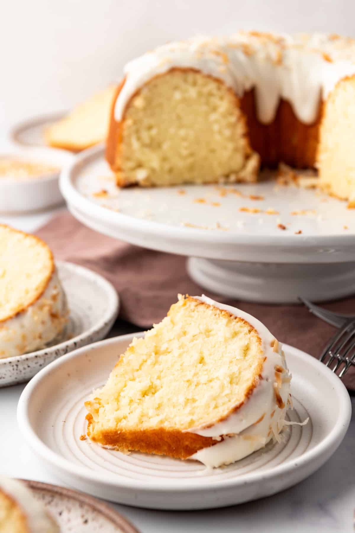 A piece of coconut bundt cake lying on its side in front of the rest of the cake.