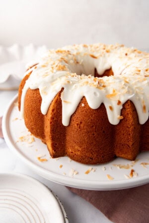 An image of a coconut bundt cake on a white cake stand.