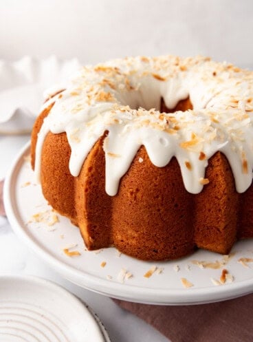 An image of a coconut bundt cake on a white cake stand.