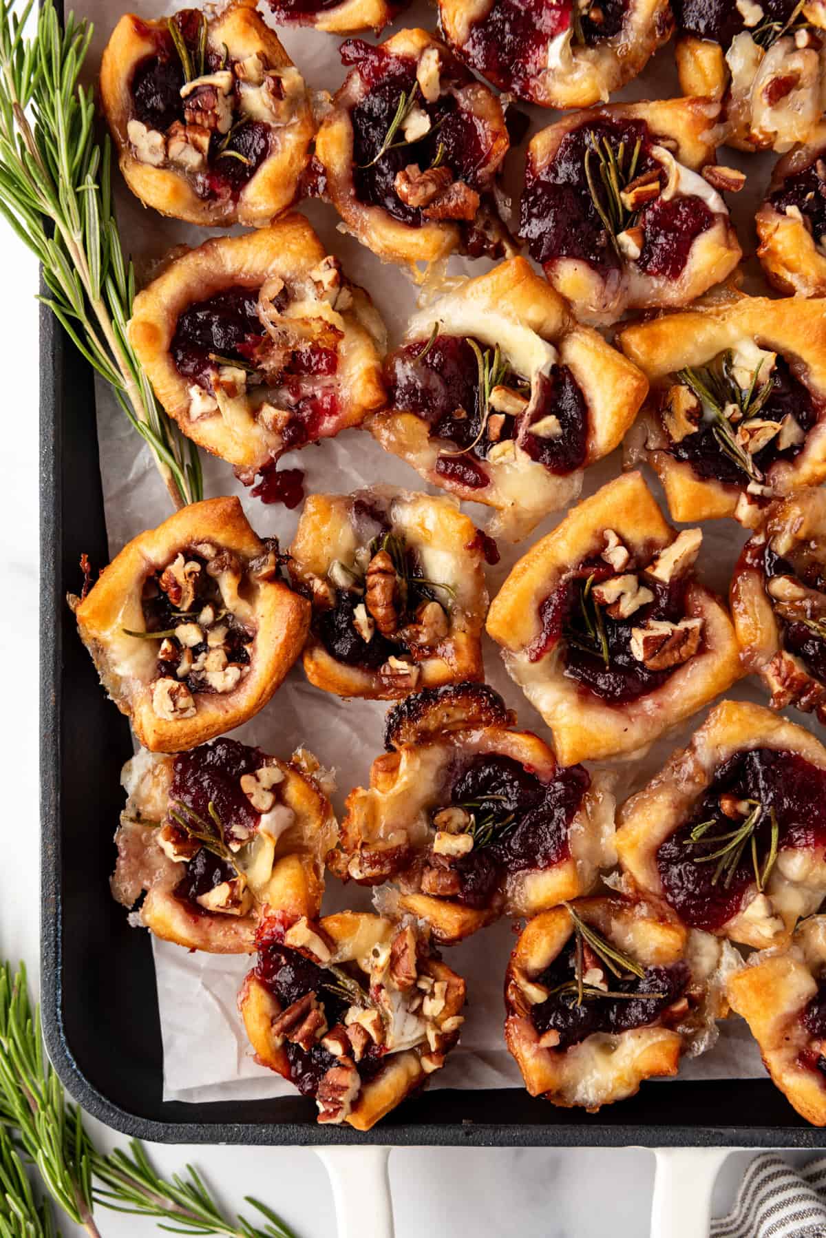 An overhead image of cranberry brie bites next to sprigs of rosemary.