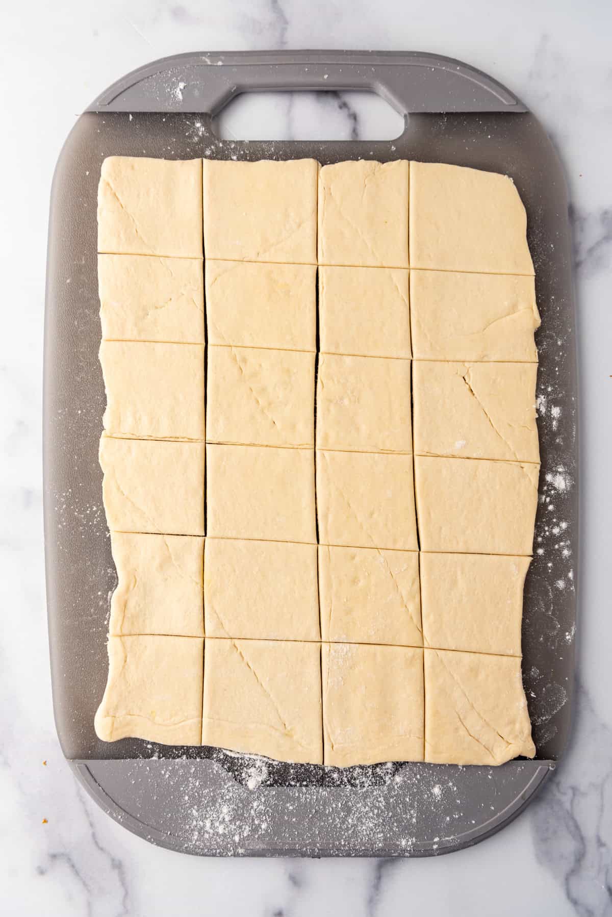 Crescent roll dough cut into 24 small squares on a cutting board.