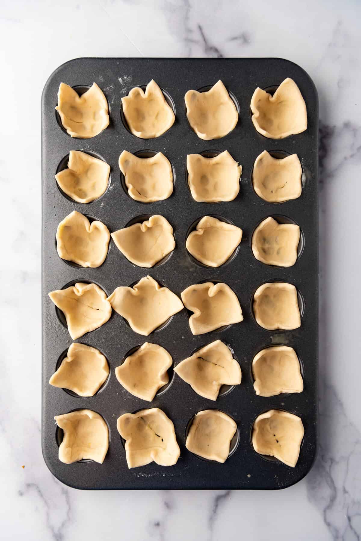 Squares of puff pastry pressed into the cups of a mini muffin pan.