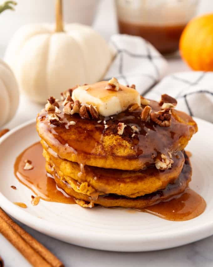 A stack of pumpkin pancakes with cinnamon syrup and chopped pecans on top.