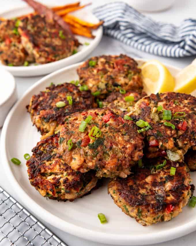 Salmon cakes on a white plate with lemon wedges in the background.