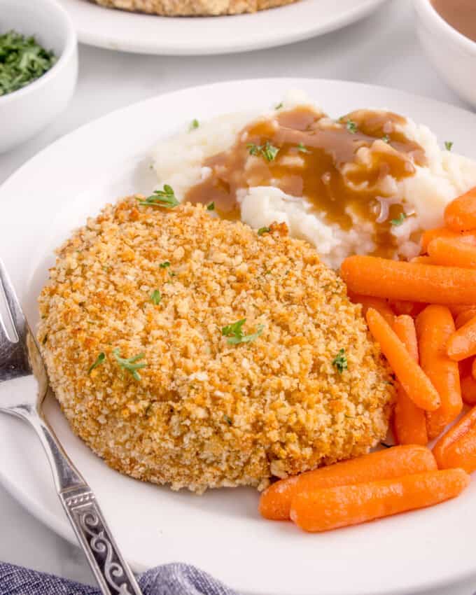 A shake n bake pork chop on a plate with mashed potatoes, gravy, and carrots.