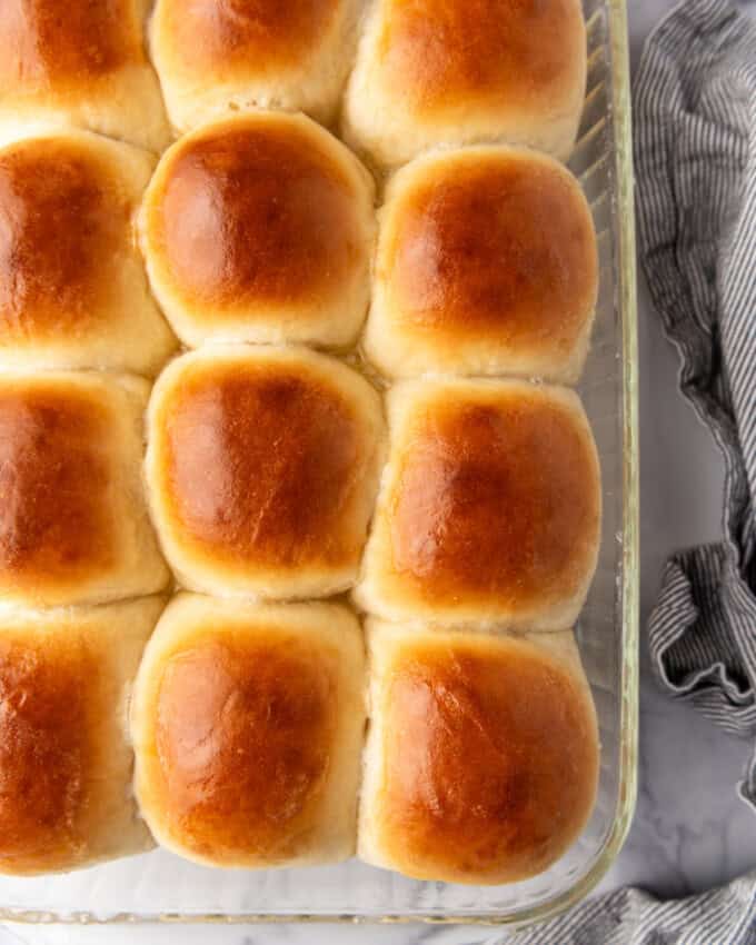 A dozen baked dinner rolls in a glass baking pan.