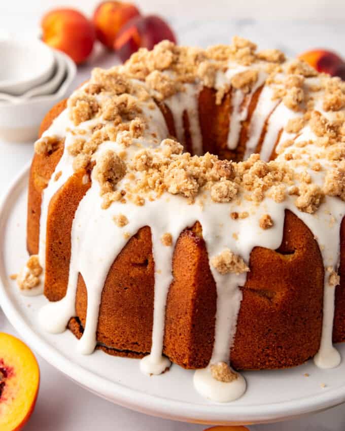 A peach cobbler pound cake with glaze and crumble topping on it.