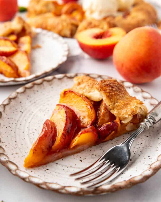 A slice of fresh peach galette on a plate with a fork.