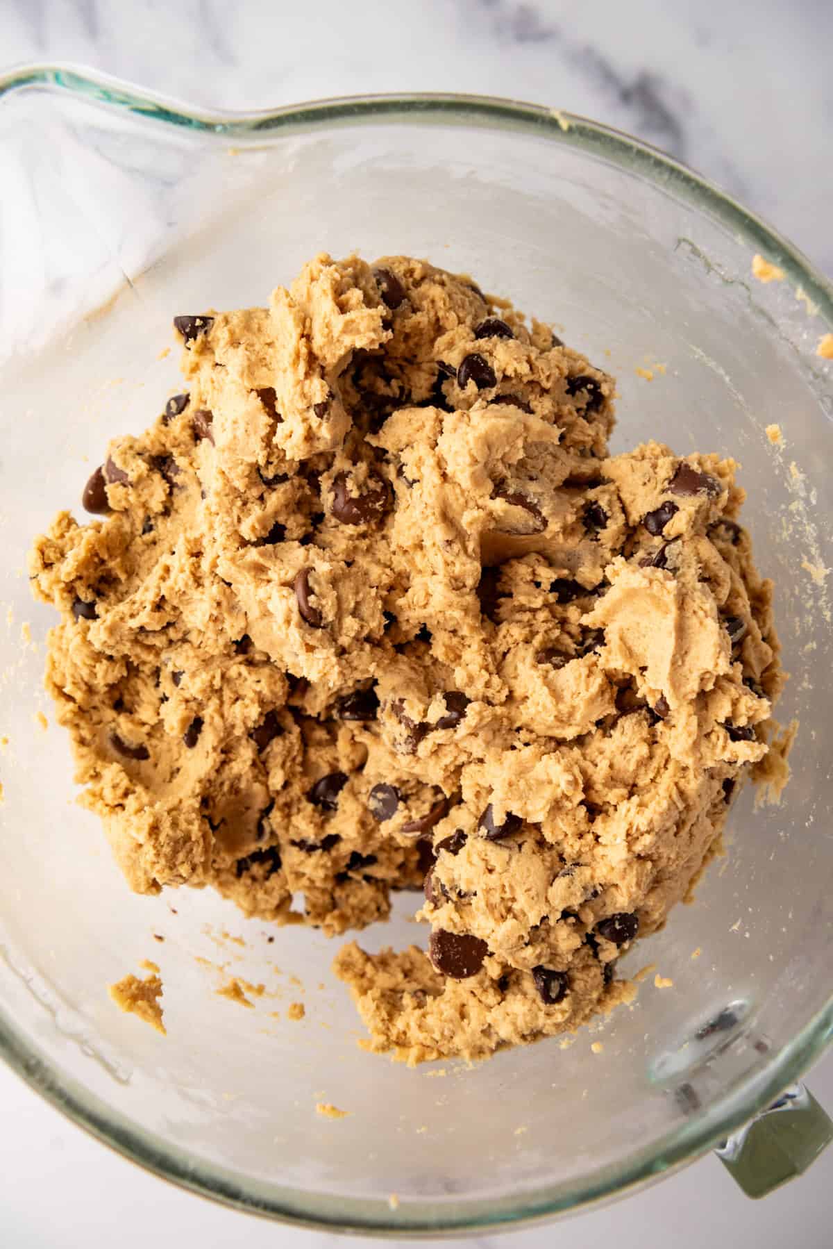 A close up image of oatmeal peanut butter chocolate chip cookie dough in a glass mixing bowl.